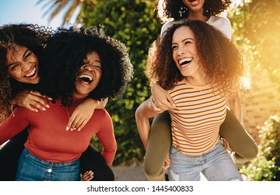 Cheerful female friends walking outdoors in city and having fun. Young women piggybacking their friends outdoors in the city.