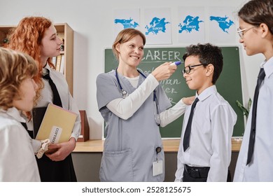 Cheerful female healthcare worker demonstrating new medical infrared thermometer to group of teen students during career day class - Powered by Shutterstock