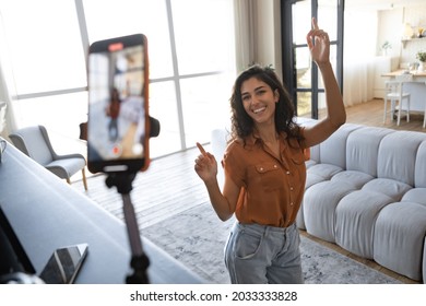 Cheerful female influencer shooting dance video for social media on mobile phone, having fun at home. Lifestyle blogger live streaming content for her vlog, broadcasting online