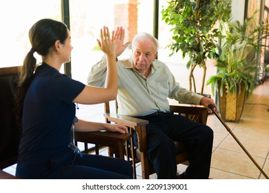 Cheerful Female Nurse And Older Man In His 80s Making A High Five And Having Fun Together While At The Nursery Home