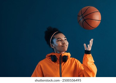 Cheerful female in orange fitness attire throw a basketball over blue background. Smiling sportswoman looking at flying basketball. - Powered by Shutterstock