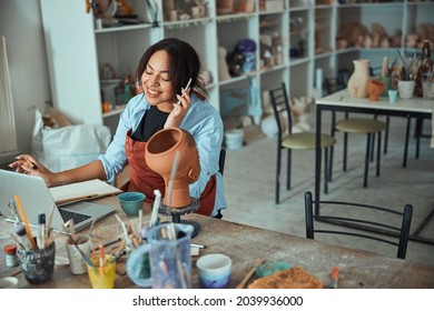 Cheerful female potter talking on cellphone in pottery workshop - Powered by Shutterstock