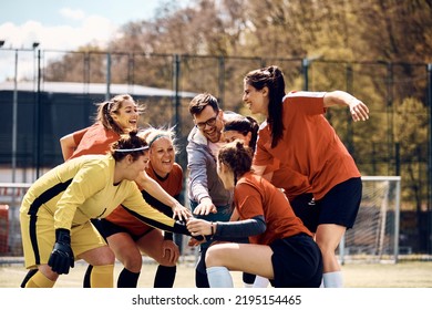 Cheerful female soccer players and their coach gathering hands in unity before the match on playing field. - Powered by Shutterstock