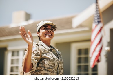 Cheerful female soldier smiling and waving her hand proudly while standing outside her home. Patriotic American servicewoman coming back home after serving her country in the military.