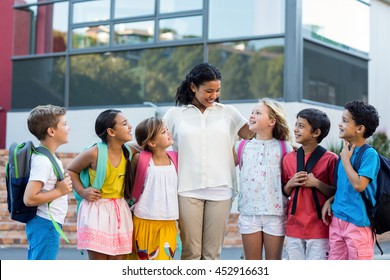 Cheerful female teacher with children standing outside school