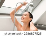 Cheerful Female Washing Holding Shower Head With Running Water Enjoying Hygiene Routine With Eyes Closed In Bathroom At Home. Woman Enjoying Taking Shower Indoor. Selective Focus