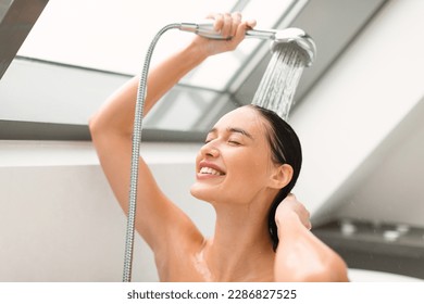 Cheerful Female Washing Holding Shower Head With Running Water Enjoying Hygiene Routine With Eyes Closed In Bathroom At Home. Woman Enjoying Taking Shower Indoor. Selective Focus - Shutterstock ID 2286827525