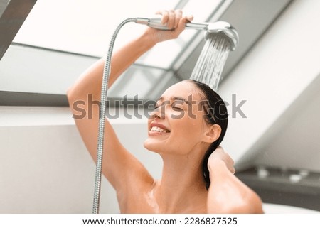 Cheerful Female Washing Holding Shower Head With Running Water Enjoying Hygiene Routine With Eyes Closed In Bathroom At Home. Woman Enjoying Taking Shower Indoor. Selective Focus