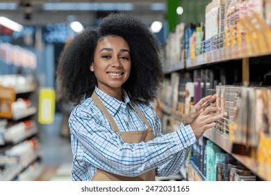 Cheerful female worker wearing an apron, arranging items on a shelf in a brightly lit supermarket aisle. - Powered by Shutterstock