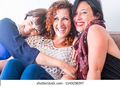 Cheerful Females Middle Age Young Womane Friends Together Sitting On A Sofa At Home In Leisure Activity Indoor. Smile And Enjoy The Day Hugging And Touching With Care And Friendship