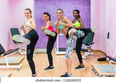 Cheerful Fit Women Holding Dumbbells, While Doing A Lateral Leg Raise During A Group Class Of Cardio Kickboxing Workout In A Trendy Fitness Centre For Ladies Only