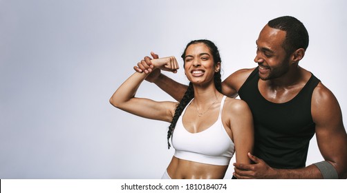 Cheerful fitness woman having fun showing biceps standing with male athlete. Fitness couple sharing happy moments after workout.