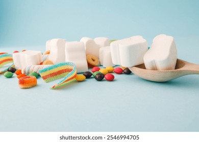 A cheerful flat lay composition of assorted colorful candies and marshmallows arranged on a light blue background. Featuring rainbow ribbon candy, white marshmallow clouds, colorful chewy balls.