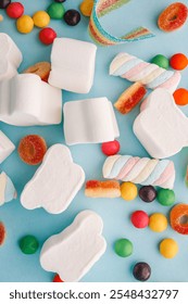 A cheerful flat lay composition of assorted colorful candies and marshmallows arranged on a light blue background. Featuring rainbow ribbon candy, white marshmallow clouds, colorful chewy balls.