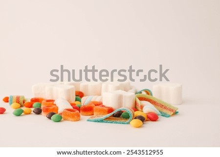 A cheerful flat lay composition of assorted colorful candies and marshmallows arranged on a light background. Featuring rainbow ribbon candy, white marshmallow clouds, colorful chewy balls.