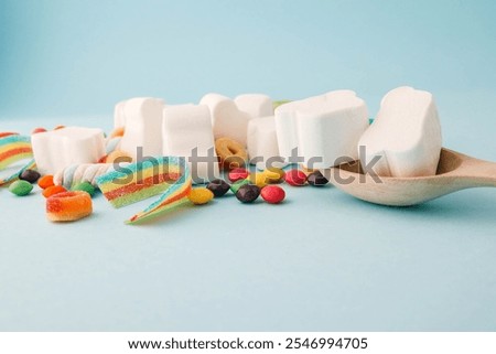 A cheerful flat lay composition of assorted colorful candies and marshmallows arranged on a light blue background. Featuring rainbow ribbon candy, white marshmallow clouds, colorful chewy balls.