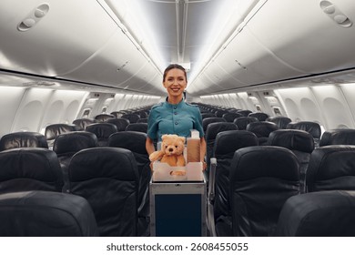 A cheerful flight attendant stands proudly with a cute teddy bear in an empty airplane cabin awaiting passengers