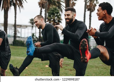 Cheerful Football Players Doing Warm Up Exercises On The Field Before The Match. Happy Footballers Doing Leg Raises Standing On The Field.