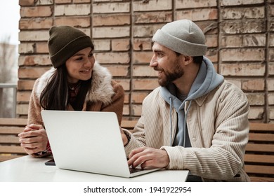 cheerful freelancer in beanie hats looking at each other near laptop