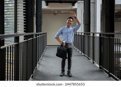 A cheerful, friendly Asian millennial businessman waving to greet his colleague while walking along the building corridor, holding a coffee cup and a briefcase. businesspeople concept - Powered by Shutterstock