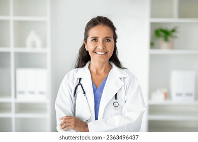 Cheerful friendly attractive long-haired mature lady wearing white medical coat with stethoscope doctor posing at clinic. Happy woman physician smiling at camera. Healthcare, medical workers - Powered by Shutterstock