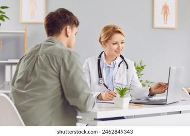 Cheerful friendly female doctor at medical office in hospital, showing examination results on laptop monitor screen and having consultation with young man patient sitting in clinic. - Powered by Shutterstock