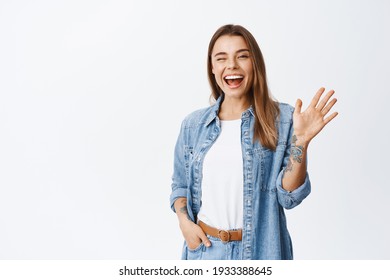 Cheerful friendly girl saying hello, winking and smiling, waving hand at camera, say hi and greet you, standing against white background - Powered by Shutterstock