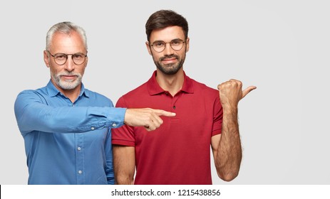 Cheerful Friendly Men Of Different Generations Involved In Advertising Campaign, Wear Spectacles, Point Together Aside, Demonstrate Something. Two Bearded Partners Show Way To Office Building