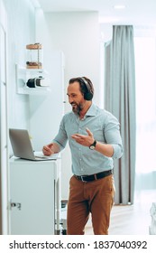 Cheerful Friendly Young Man Standing In Front Of A Laptop Screen In The Bedroom And Gesturing At The Online Meeting