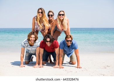 Cheerful friends forming pyramid on shore at beach during sunny day - Powered by Shutterstock