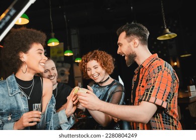 Cheerful friends holding lime and tequila near african american friend in bar - Powered by Shutterstock