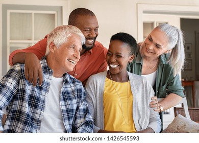 Cheerful Friends Sitting In Courtyard Enjoying Afternoon Together. Group Of Four Mature People Sitting Outside Home And Laughing. Happy Senior Man And Old Woman Enjoying With Mature African Couple.