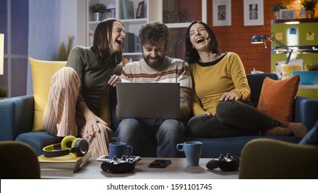 Cheerful friends sitting on the sofa at home and connecting online with their laptop, they are social networking and having fun