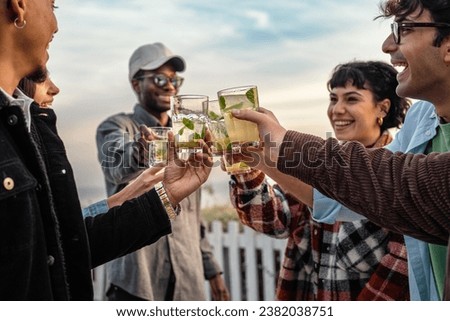 Cheerful friends with summer drinks - Joyful group of friends raising glasses filled with refreshing drinks, toasting to a good time outdoors with a clear sky backdrop.