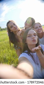 Cheerful friends take a selfie in the meadow and blow a kiss.