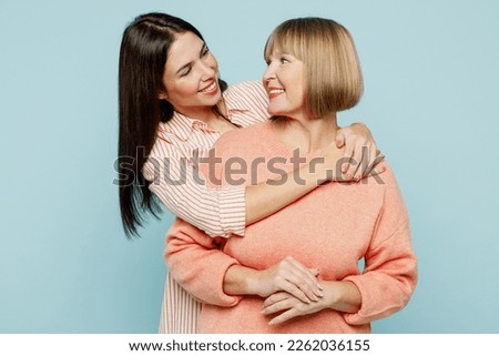 Cheerful fun satisfied elder parent mom with young adult daughter two women together wearing casual clothes hugging cuddle look to each other isolated on plain blue cyan background. Family day concept