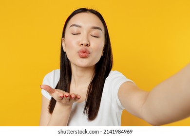 Cheerful Fun Young Girl Woman Of Asian Ethnicity 20s Years Old Wears White T-shirt Doing Selfie Shot Pov On Mobile Phone Blowing Sending Air Kiss Isolated On Plain Yellow Background Studio Portrait