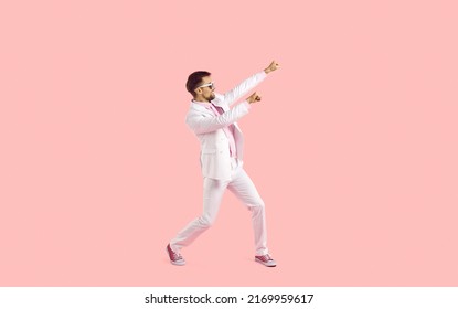 Cheerful Funny And Active Young Man In Suit Having Fun Isolated On Pastel Pink Background. Stylish Man In White Formal Suit, Sneakers And Glasses Cheerfully Waving His Arms. Full Length. Copy Space.