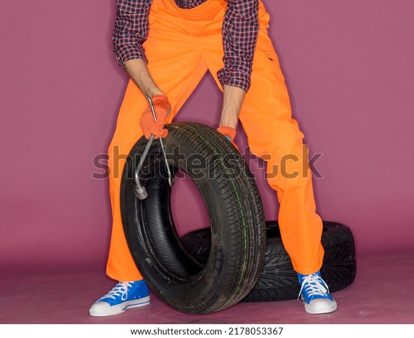 cheerful funny auto mechanic with wheel\
and tools.technician in orange overalls on lilac background.auto\
business car service\
concept.isolated.