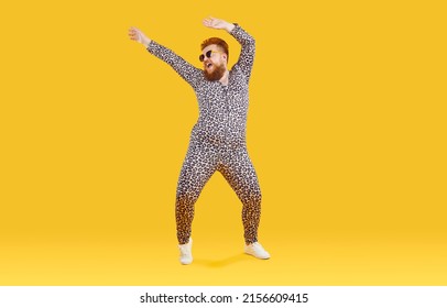Cheerful funny eccentric fat man in good mood is dancing and fooling around on orange background. Overweight bearded man dressed in leopard print jumpsuit is dancing and fooling around. Full length. - Shutterstock ID 2156609415