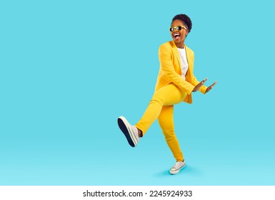 Cheerful, funny and energetic African American woman having fun dancing in studio. Crazy woman in yellow casual suit having fun near copy space on light blue background. Isolated. Full length. Banner. - Shutterstock ID 2245924933