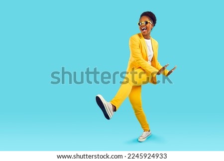 Cheerful, funny and energetic African American woman having fun dancing in studio. Crazy woman in yellow casual suit having fun near copy space on light blue background. Isolated. Full length. Banner.