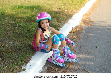 A cheerful funny laughing girl with pink pigtails in a protective helmet and roller skates sat down to rest after training. Summer vacations with benefits.