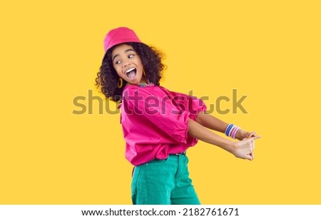 Cheerful funny stylish african american teen girl having fun on vivid yellow background. Happy energetic kid girl in trendy bright colored clothes having fun and fooling around laughing out loud.