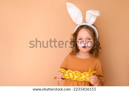 A cheerful funny surprised girl with an open mouth shouts in greeting to the new year 2023. A child disguised as rabbit is symbol of the year according to Chinese calendar