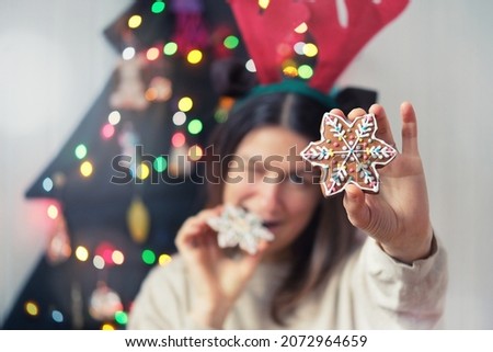 Cheerful funny woman showing to camera x-mas gingerbread snowflake shaped cookies near alternative christmas tree. Depth of field.