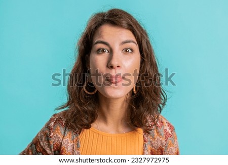 Cheerful funny young woman showing tongue making faces at camera, fooling around, joking, aping with silly face, teasing, bullying, abuse. Girl isolated alone on blue studio background. Lifestyles