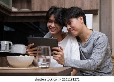 Cheerful gay couple embracing and using digital tablet together in their kitchen. LGBT and love concept. - Powered by Shutterstock