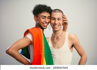 Cheerful gay couple with pride flag on white background. Two homosexual men standing together and smiling.