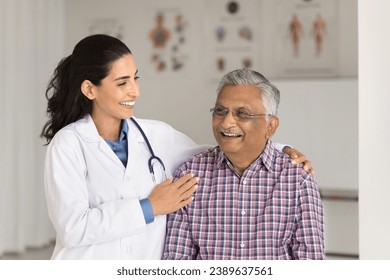 Cheerful geriatrician woman and old Indian patient laughing in clinic office together, talking, discussing good news, successful therapy, treatment. Doctor touching mans shoulders with care - Powered by Shutterstock